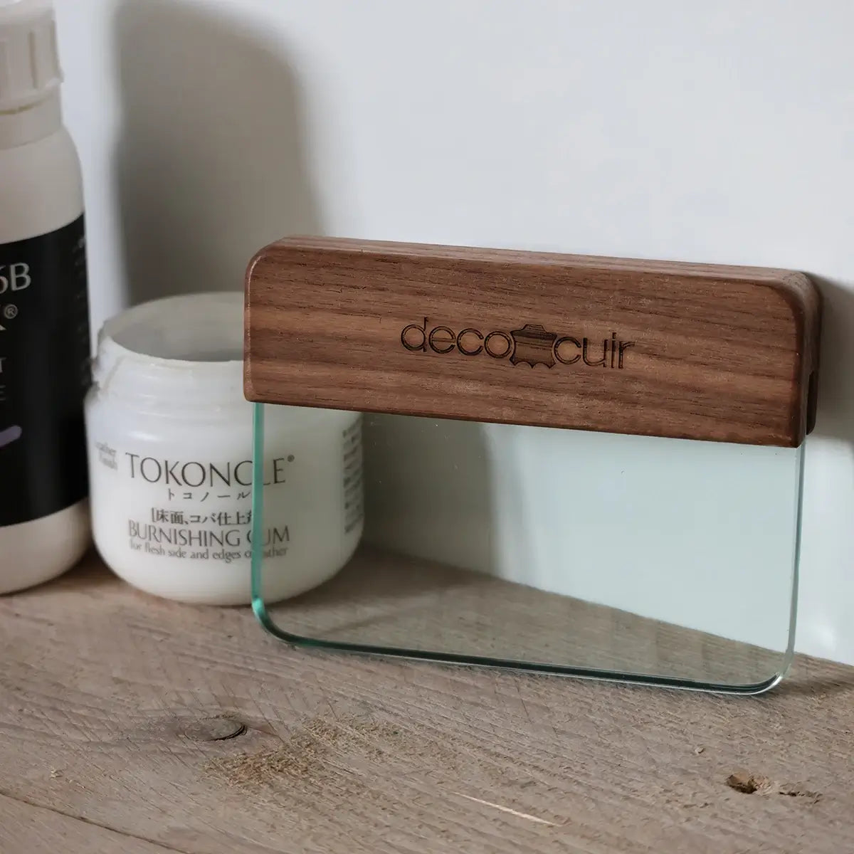 Lisseur en verre trempé avec manche en bois pour travailler le cuir, fabriqué par Deco Cuir, posé sur une surface en cuir.