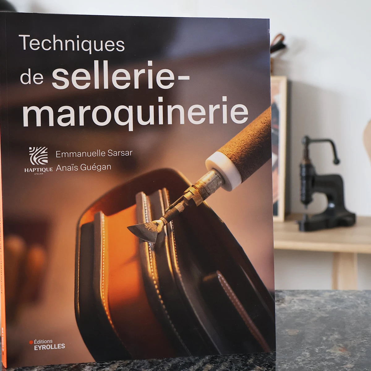 Livre "Techniques de sellerie-maroquinerie" d'Emmanuelle Sarsar et Anaïs Guégan, avec illustrations et pages ouvertes.